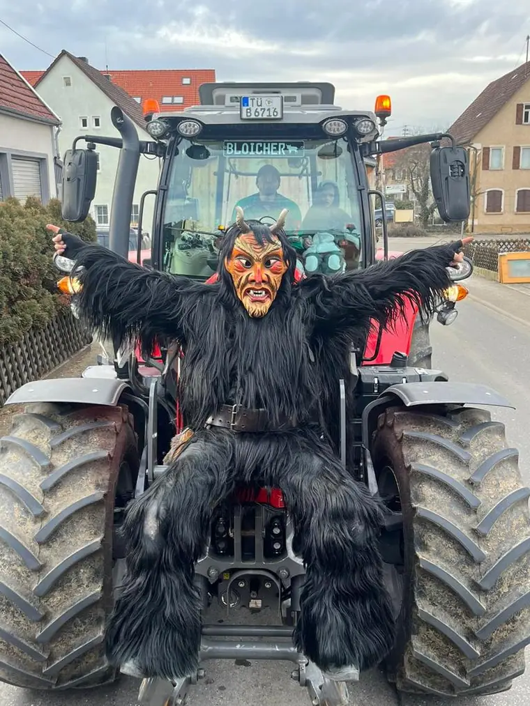 Teufel im schwarzen Fellhäs vor einem Traktor